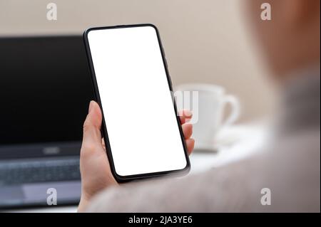 Scatto corto della donna d'affari che guarda lo smartphone a schermo vuoto nella stanza d'ufficio moderna. Donna mano che tiene il telefono con schermo bianco in ufficio. Donna noi Foto Stock