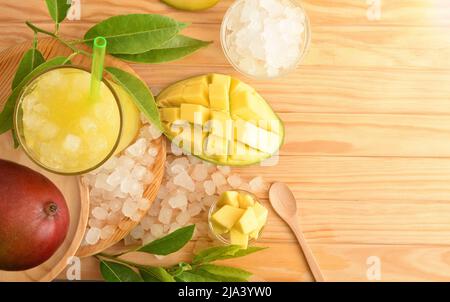 Particolare di un bicchiere con succo di mango con ghiaccio su un tavolo di legno con frutta e ghiaccio tritato intorno ad esso. Vista dall'alto. Composizione orizzontale. Foto Stock