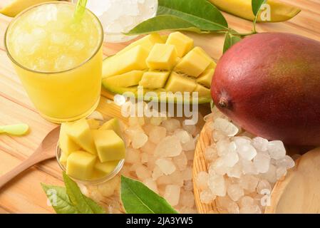 Particolare di un bicchiere con succo di mango con ghiaccio su un tavolo di legno con frutta e cubetti intorno ad esso. Vista dall'alto. Composizione orizzontale. Foto Stock