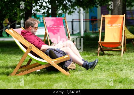 Hay Festival, Hay on Wye, Galles, Regno Unito – Venerdì 27th Maggio 2022 – Un visitatore ha la possibilità di sedersi e leggere al sole sui prati del Festival tra gli eventi durante il secondo giorno di questo anno Hay Festival – questa è la prima volta che l'evento si svolge di persona dal 2019. Il Festival di Hay si svolge fino al 5th giugno 2022. Foto Steven Maggio / Alamy Live News Foto Stock