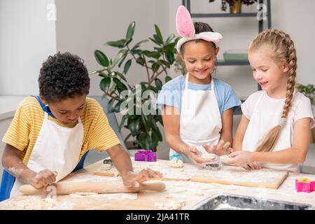 Carino piccolo ragazzo setacciare la farina permanente, mentre dalla tabella accanto alla sua mamma e preparare l'impasto per dolci fatti in casa Foto Stock