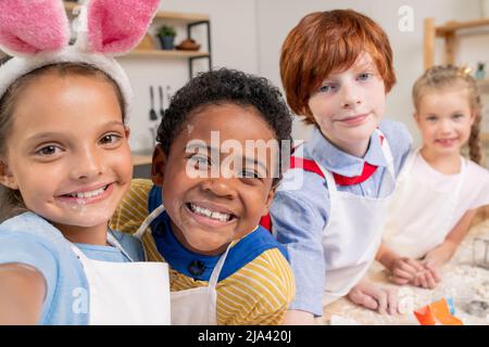 Ragazzo carino e sua madre di pasta di rotolamento durante la cottura di dolci fatti in casa da tavolo in cucina Foto Stock