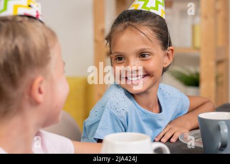 Ragazze carine seduti al tavolo e bere il tè, mescolando farina e uova in una ciotola d'acciaio di fronte alla macchina fotografica in cucina ambiente Foto Stock