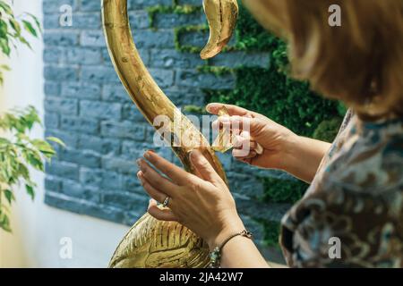 Una donna designer ripristina e copre una statuetta in legno fenicottero con lamina d'oro. Il processo di doratura manuale Foto Stock