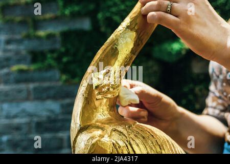 Una donna designer ripristina e copre una statuetta in legno fenicottero con lamina d'oro. Il processo di doratura manuale Foto Stock