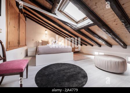 camera da letto in mansarda con soffitti inclinati con travi in legno d'epoca e lucernario bianco in alluminio Foto Stock