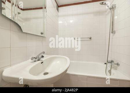 Bagno con lavello in porcellana bianca e piccola vasca con rubinetti cromati Foto Stock