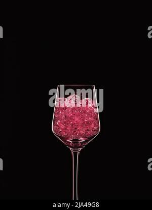 Bicchiere da vino riempito con cristalli rosa trasparenti retroilluminati e isolati su sfondo nero. Concetto di vetreria per bevande. Spazio di copia. Foto Stock