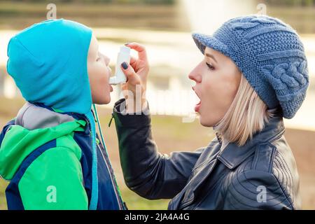 Donna che usa un inalatore di asma al suo figlio in un freddo inverno autunno Parco Foto Stock