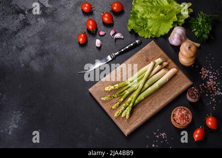 Un mazzo di rami di asparagi crudi freschi verdi su un tagliere di legno su un fondo di cemento scuro Foto Stock