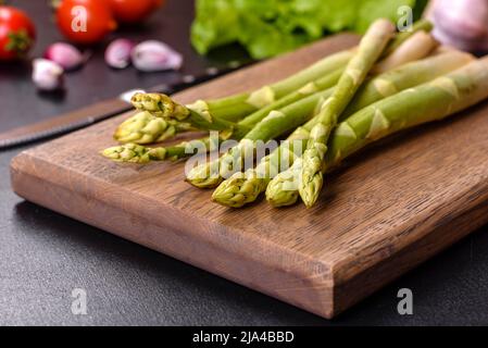 Un mazzo di rami di asparagi crudi freschi verdi su un tagliere di legno su un fondo di cemento scuro Foto Stock