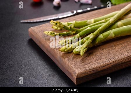 Un mazzo di rami di asparagi crudi freschi verdi su un tagliere di legno su un fondo di cemento scuro Foto Stock