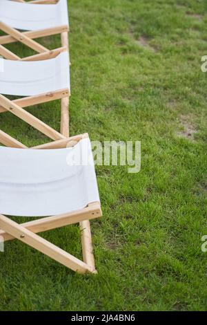 Parte di una sedia pieghevole leggera per attività ricreative all'aperto. Una chaise longue bianca vuota in legno sull'erba verde di un prato fresco con un posto da copiare. Foto di alta qualità Foto Stock