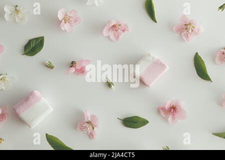 Disegno creativo composto da vari fiori di primavera, foglie e marshmallows. Fondo naturale piatto. Foto Stock
