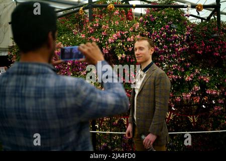 Un visitatore si pone per una fotografia di fronte ad una mostra floreale nel Grande Padiglione al RHS Chelsea Flower Show, al Royal Hospital Chelsea, Londra. Data foto: Venerdì 27 maggio 2022. Foto Stock