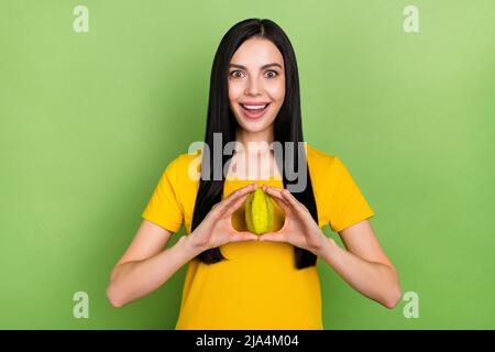 Foto di donna dolce impressionato indossare giallo t-shirt tenendo frutti tropicali isolato verde sfondo di colore Foto Stock