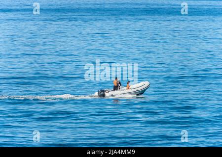 Piccolo gommone (motoscafo) in movimento con sveglia nel blu del Mediterraneo con due persone a bordo in una soleggiata giornata estiva, Liguria, Italia. Foto Stock