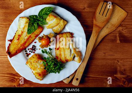 Filetti di merluzzo su un piatto bianco con finocchio ed erbe su un pannello di legno, Foto Stock