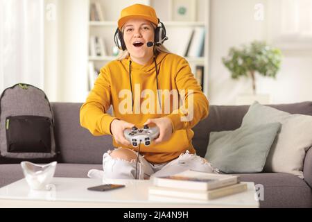 Donna eccitata con cuffie e un joystick seduto su un divano e giocare a videogiochi a casa Foto Stock