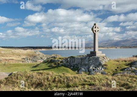 Veduta della Croce Celtica sull'Isola di Ynys Llanddwyn ad Angelsey con montagne innevate sullo sfondo distante Foto Stock