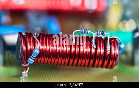 Bobina elettronica - nucleo in ferrite e piccole resistenze blu con codice colore su filo di rame rosso. Induttore elettromagnetico cilindrico. Dettaglio PCB dell'amplificatore TV via cavo. Foto Stock