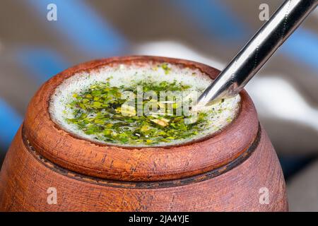 Coppa di legno di giallo caldo mate con bombilla metallo paglia dettaglio. Foglie di agrifoglio verde essiccato e schiuma bianca in tisane. Tradizionale bevanda sudamericana. Foto Stock