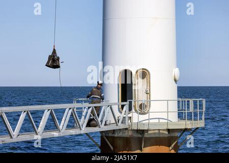 Lelystad, Paesi Bassi - 22 aprile 2022: Lavoratori edili impegnati nel sollevamento di un set di strumenti per la manutenzione di una turbina eolica Foto Stock