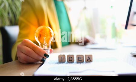 Donna d'affari in tuta verde che tiene lampadina sopra idea closeup parola Foto Stock