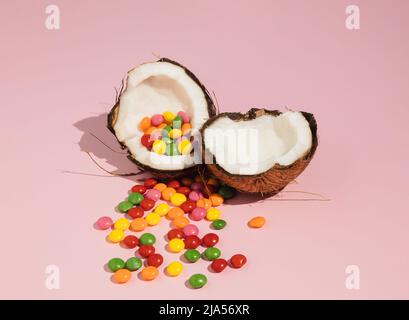 Cocco incrinato a metà e caramelle colorate. Un'idea estiva minima. Concetto di cibo creativo. Foto Stock