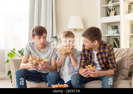 Un carino tre ragazzi adolescenti, mangiando fast food in soggiorno Foto Stock