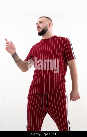 Ritratto verticale di brunetto tatuato uomo sicuro in posa. Indossalo sportivo rosso informale. Dito puntato gesturante Foto Stock