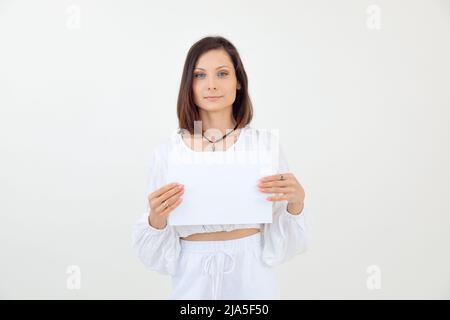 Donna sorridente e sicura dai capelli marroni in abiti bianchi con promo modello, banner per testo. Spazio di copia Foto Stock