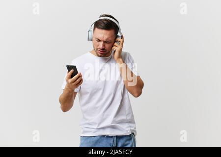 Happy concentrato rilassante abbronzato bell'uomo in base t-shirt cuffie mobili godere fresco rock canzone posa isolato su su bianco studio Foto Stock