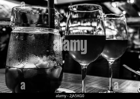 Una caraffa di sangria accompagnata da due bicchieri allineati su un tavolo di legno (bianco e nero). Foto Stock