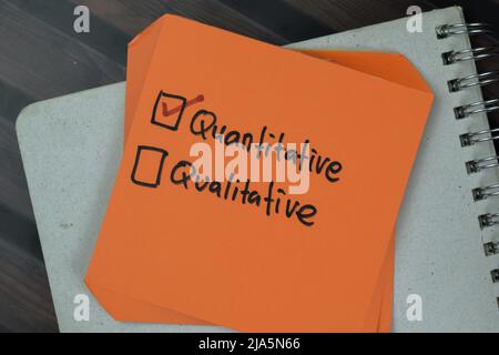 Concetto di scrittura quantitativa o qualitativa su note adesive isolate su tavola di legno. Foto Stock