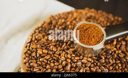 Caffè macinato in portafiltro su asse di legno con chicchi di caffè. Caffè appena macinato in portafiltro e fagioli tostati per la preparazione di fragranti d Foto Stock