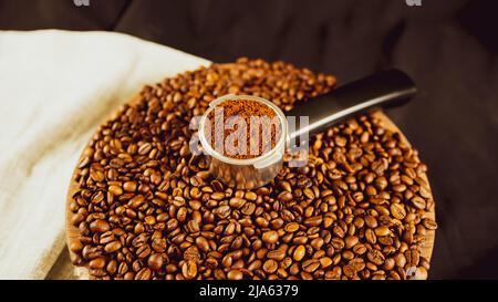 Caffè macinato in portafiltro su asse di legno con chicchi di caffè. Caffè appena macinato in portafiltro e fagioli tostati per la preparazione di fragranti d Foto Stock