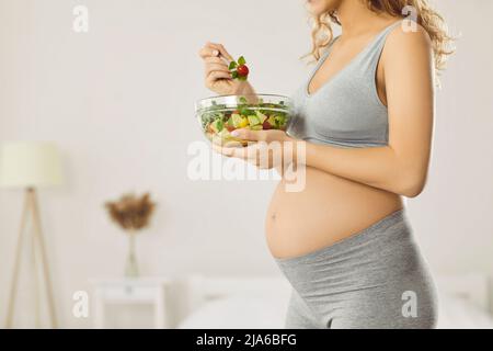 La donna incinta con il ventre grande si prende cura della sua salute e mangia insalate di verdure fresche Foto Stock