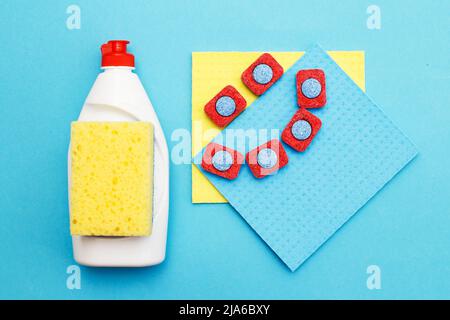 capsule per lavastoviglie, detersivi liquidi per lavastoviglie, straccio da cucina e spugne su fondo blu. piatto Foto Stock