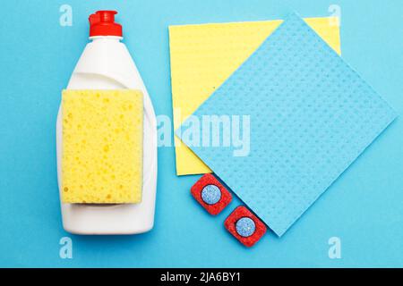 capsule per lavastoviglie, detersivi liquidi per lavastoviglie, straccio da cucina e spugne su fondo blu. piatto Foto Stock