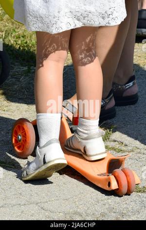 Piedi ragazze primo piano su uno scooter. Scooter per bambini. Giro di sicurezza su uno scooter per bambini. Foto verticale. Primo piano. Foto Stock