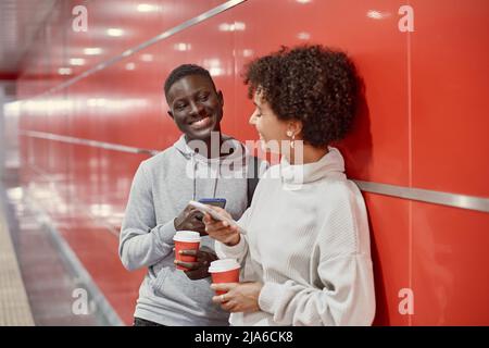 giovani con smartphone e caffè da asporto in attesa del treno della metropolitana . Foto Stock