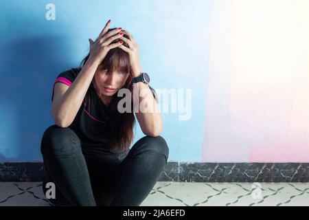 Donna disperata in depressione si siede contro il muro con la testa giù sulle sue ginocchia. Concetto di problemi mentali e salute mentale. Foto Stock