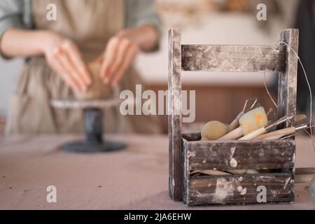 Il primo piano di una mano di una donna artigiana che lavora con argilla in un laboratorio di ceramica indossando un grembiule crea una ciotola di ceramica fatta a mano. Il concetto di abilità e. Foto Stock