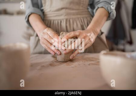 Fai da te il primo piano di un vasaio femminile che scolpisce l'argilla prima di modellare la ceramica in un laboratorio di ceramica durante un'officina. Il concetto di artigianato e. Foto Stock