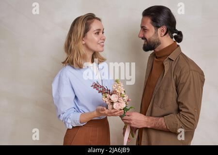 Ritratto di romantico giovane uomo che dà bei fiori alla sua ragazza attraente per San Valentino Foto Stock