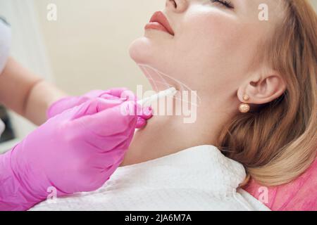 Le mani del medico nei guanti rosa sta facendo i segni sul mento del cliente nel centro di bellezza Foto Stock