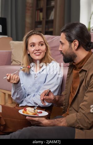 Giovane uomo alla moda e bella donna bionda che passa la mattina insieme seduto sul pavimento in soggiorno per fare colazione e chiacchierare Foto Stock