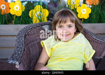 La ragazza felice siede in una sedia di vimini. Foto Stock