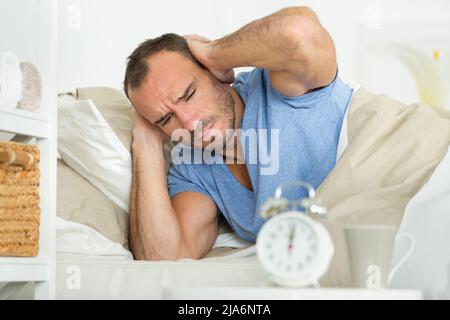 uomo a letto che copre le orecchie mentre suona la sveglia Foto Stock